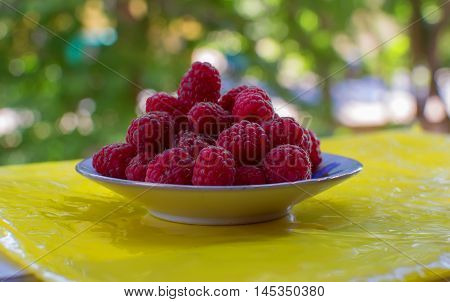 The saucer with fresh,sweet raspberries hill on the table