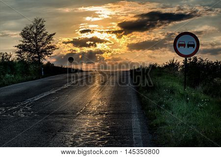 No overtaking sign by an old and damaged road in a dramatic sunset