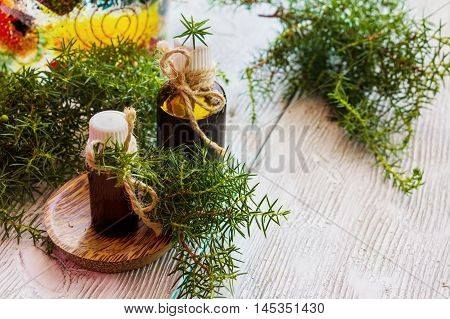 Juniper essential oil in a glass bottle on a wooden table. Used in medicine cosmetics and aromatherapy. Fresh green sprigs. Selective focus.