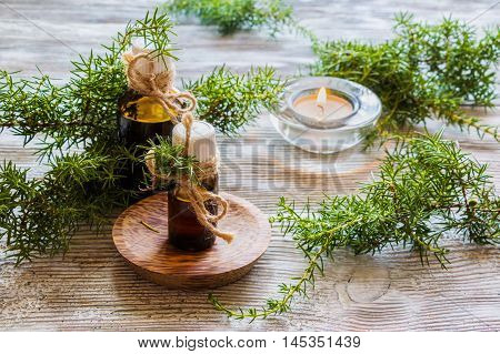 Juniper essential oil in a glass bottle on a wooden table. Used in medicine cosmetics and aromatherapy. Fresh green sprigs and burning candle. Selective focus.