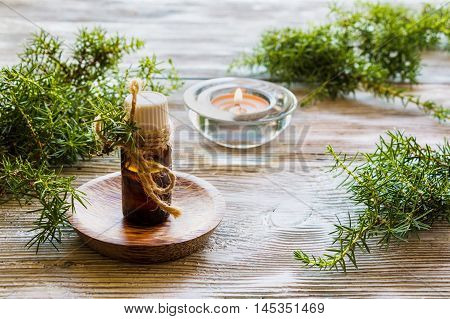 Juniper essential oil in a glass bottle on a wooden table. Used in medicine cosmetics and aromatherapy. Fresh green sprigs and burning candle. Selective focus.