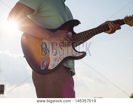 young man standing with a guitar on a background of sky and sunlight