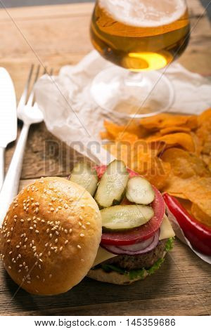 Beef burger with lettuce and minced meat cutlet. Potato chips and glass of beer