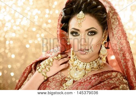 Pretty girl in traditional Indian Pakistani bridal costume with heavy makeup and jewellery against a glittery background