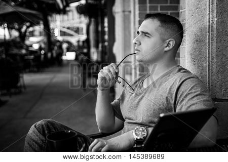 Man with glasses arm on chin thinking deep thoughts and making tough decision, sitting at cafe with I pad on table.