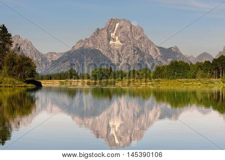 Beautiful Grand Teton mountain flecting on a smooth water surface with moonset behind the rock mountain. Oxbow Bend famous scenic point in Grand Teton National Park Wyoming USA.