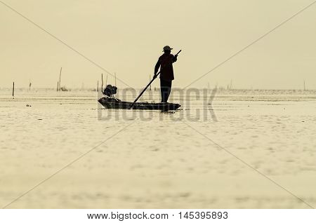 Asian fisherman on wooden boat casting a net for catching freshwater fish in nature river in the early morning before sunrise