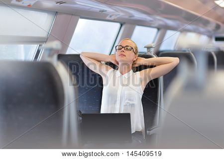 Businesswoman traveling by train, streching on her seat while working on laptop. Business travel concept.