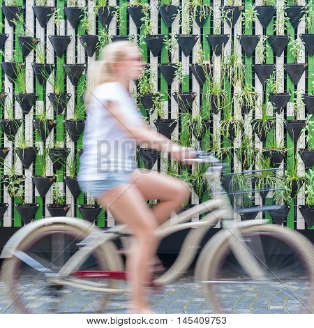 Motion blure of woman riding bycicle by green urban vertical garden wall in Ljubljana, European green capital of Europe 2016. Sustainable green city concept.