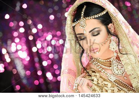 A pretty young female model wearing traditional indian pakistani bridal outfit with heavy jewelry and makeup