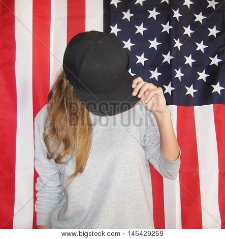 Vintage lifestyle portrait of young hipster girl against american flag background dressed in casual clothes gray blank pullover and black snapback cap