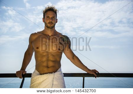 Muscular young man leaning on metal hand-railing on cruise ship, looking at camera