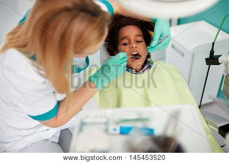 Female dentist repair tooth to nice black kid in dental practice