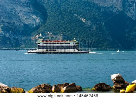 Ferry boat with tourists during navigation on Lake Garda near Malcesine Veneto Italy. In the background the coast of Lombardy