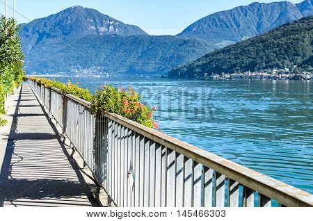 Panoramic landscape summer view of beautiful serene blue Lugano lake under clear blue sky surrounded by mountains on sunny day in Morcote Switzerland selective focus