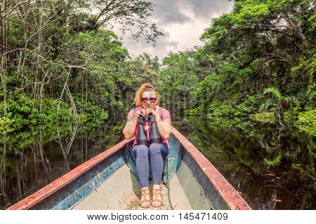 Happy Tourist Woman In A Canoe With High Power Binocular In Amazonian Jungle National Park Cuyabeno South America