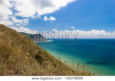 Beautiful mountain view on Black sea beach from the top of hilll. Azure water, blue cloudy sky. Hill with dry grass in foreground.