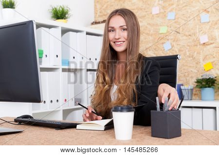 Portrait of successful business lady at her workplace in big company office. Bookcase and stickers on cork board on background. Concept of female leader