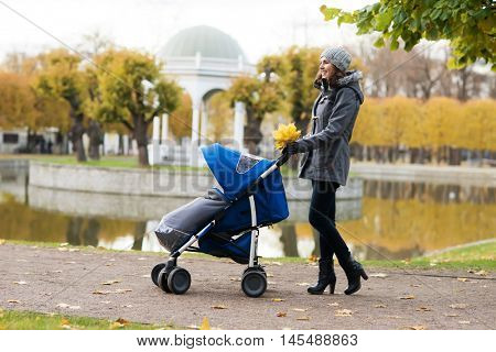 Mother walking with a baby pram (stroller, carriage) in the park. Autumn nature background. Love and family concept.