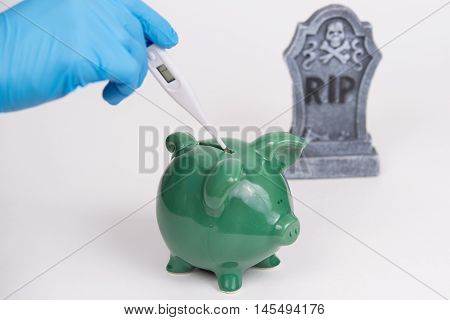 a thermometer with tombstone in background, piggy bank, and white backdrop.
