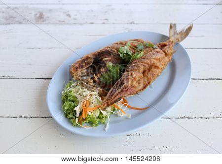 Fried Seriola fish in blue dish on wooden background.