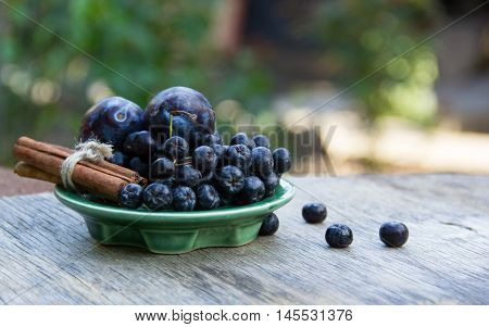 Black chokeberry (Aronia melanocarpa) and plums on wooden table. Home atmosphere. Autumn concept. Autumn harvest