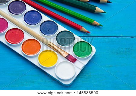Watercolors and pencils on blue wooden background. drawing tools