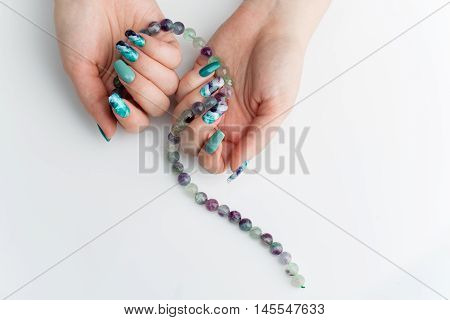 Closeup of woman nails with creative purple and green manicure. Fluorinit print. Natural stone beads. Copy space.