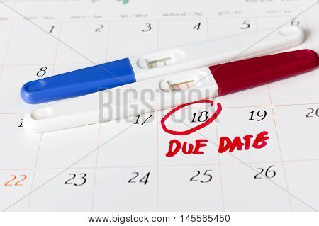 Pregnancy test with positive result lying on calendar background.circle due date 18th soft focus.
