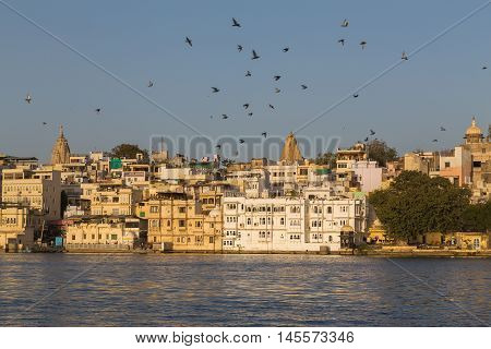 UDAIPUR INDIA - 20TH MARCH 2016: A view of part of the City of Udaipur at the lake waterfront during the day close to sunset. People birds and boats can be seen.