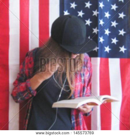 Blurred lifestyle portrait of young teenage girl standing against  isolated american flag background dressed in casual clothes black plain t-shirt, red plaid shirt, black snapback cap with hair down