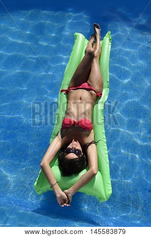 young happy beautiful woman in bikini and sunglasses lying relax on float airbed at vacation hotel resort swimming pool in Summer enjoying holidays having sunbath with tan body