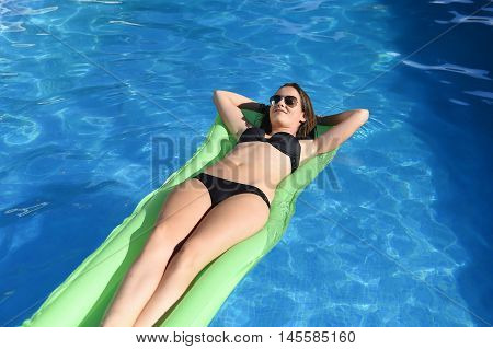 young happy beautiful woman in bikini and sunglasses lying relax on float airbed at vacation hotel resort swimming pool in Summer enjoying holidays having sunbath with tan body