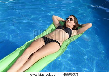 young happy beautiful woman in bikini and sunglasses lying relax on float airbed at vacation hotel resort swimming pool in Summer enjoying holidays having sunbath with tan body