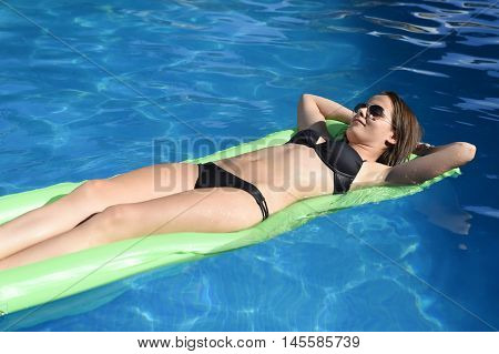 young happy beautiful woman in bikini and sunglasses lying relax on float airbed at vacation hotel resort swimming pool in Summer enjoying holidays having sunbath with tan body