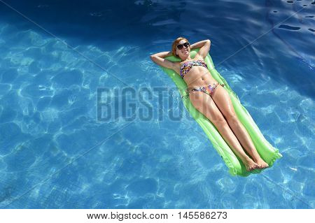 young happy beautiful woman in bikini and sunglasses lying relax on float airbed at vacation hotel resort swimming pool in Summer enjoying holidays having sunbath with copy space for text