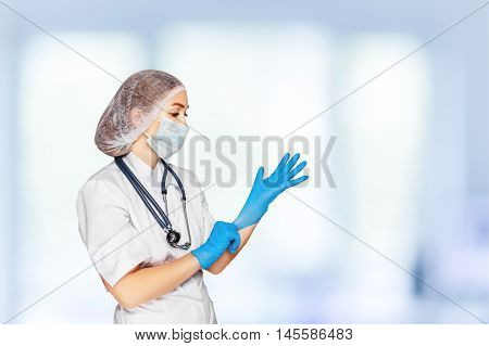 Medical surgeon doctor woman over blue clinic background. Doctor putting on sterile gloves. Place for medical advertise, medical advertising concept.