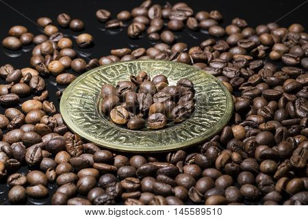 Coffee beans in gold plate on black background.