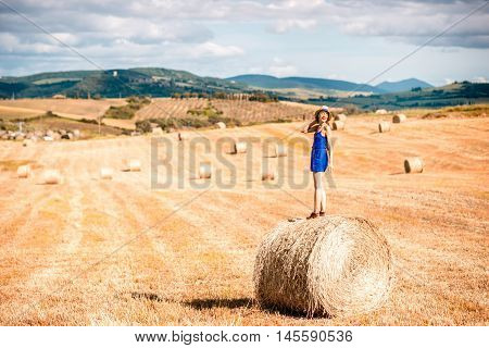 Young woman in blue dress enjoying nature on the hayfield in Tuscany in Italy
