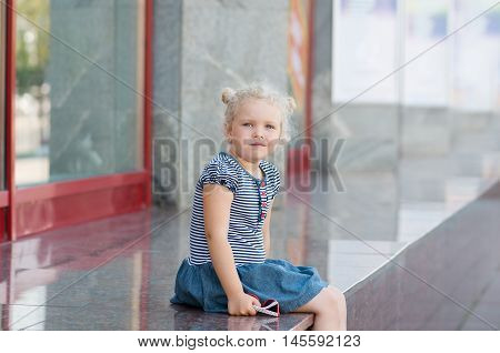 Caucasian girl 5 years old curly-haired blond sitting near the glass storefront