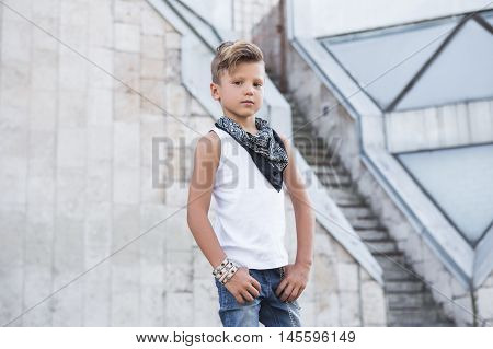 Stylish little boy put his hands in his pockets and looking forward . He has cool hair . Street fashion