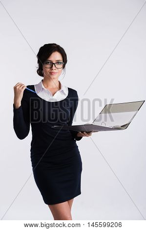 Young Caucasian woman wearing a dark blue dresst and and a white shirt, holding a ring binder folder and pen. Isolated on light background