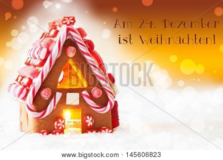 Gingerbread House In Snowy Scenery As Christmas Decoration. Candlelight For Romantic Atmosphere. Golden Background With Bokeh Effect. German Text Am 24. Dezember Ist Weihnachten Means Merry Christmas