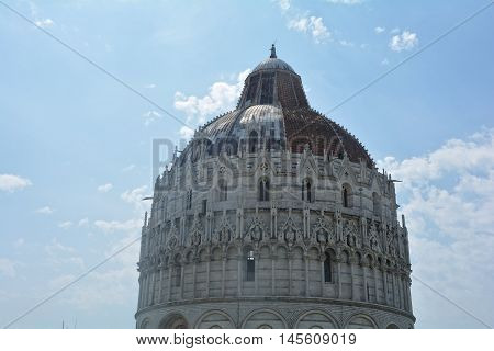 View of Baptisery building in Cathedral Square in Pisa, Italy, on cloudy blue sky background.