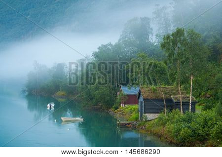 Sunrize on a foggy lake in Norway. Old houses and boats