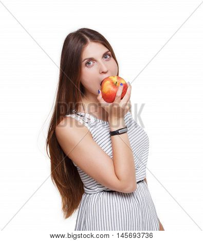 Beautiful long-haired young woman eats big ripe red apple. Female portrait isolated on white background. Girl bites fruit, hand with fitness tracker bracelet, healthy food and diet concept.