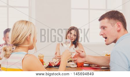 Surprised man and blond woman at dinner table, party for friends indoors at cafe or home. Friendship, relationship, relax at holidays and week-end. People sitting at table, saying toast