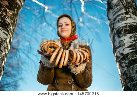 young beautiful woman in national russian suite show bagels at sunny winter day between birches.
