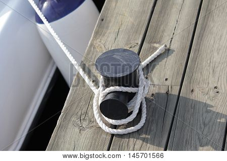 Mooring rope with a knotted end tied around a cleat on a wooden pier