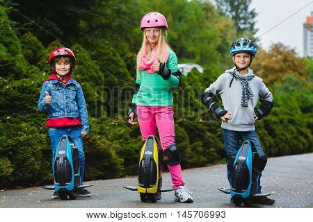 Happy kids standing near mono-wheel hoverboard or gyroscooter outdoor.